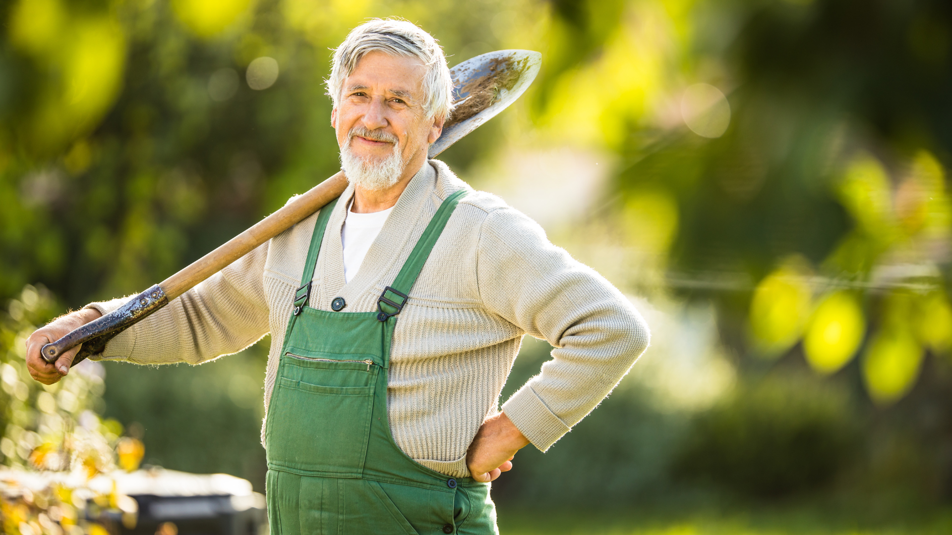 A senior man smiling carrying a shovel