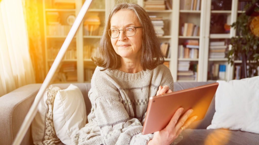 A senior woman looking at the window while holding her smart tablet