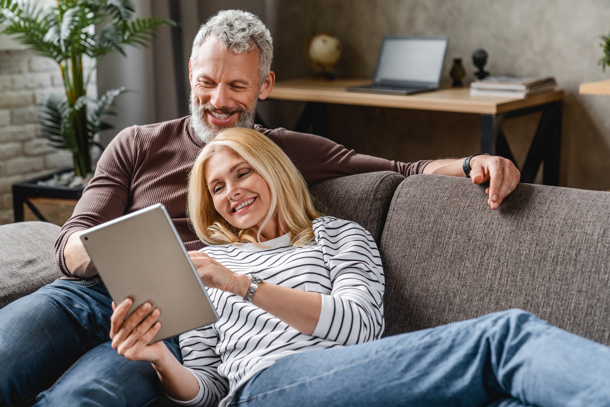 Happy senior couple using digital tablet on sofa indoors Happy senior couple using digital tablet on sofa indoors