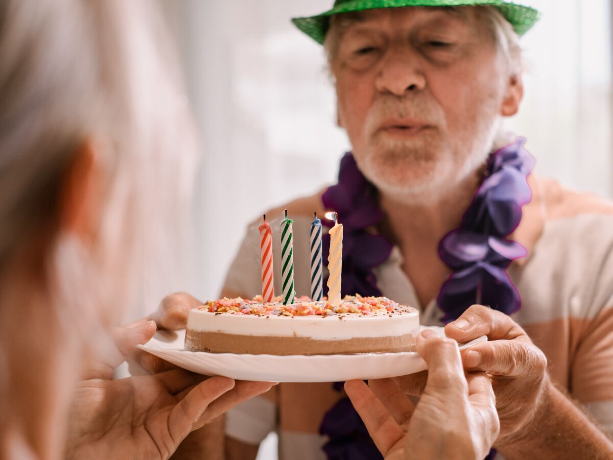 Senior man in a green party hat blowing out birthday candles, celebrating turning 65—symbolizing Medicare enrollment milestone.
