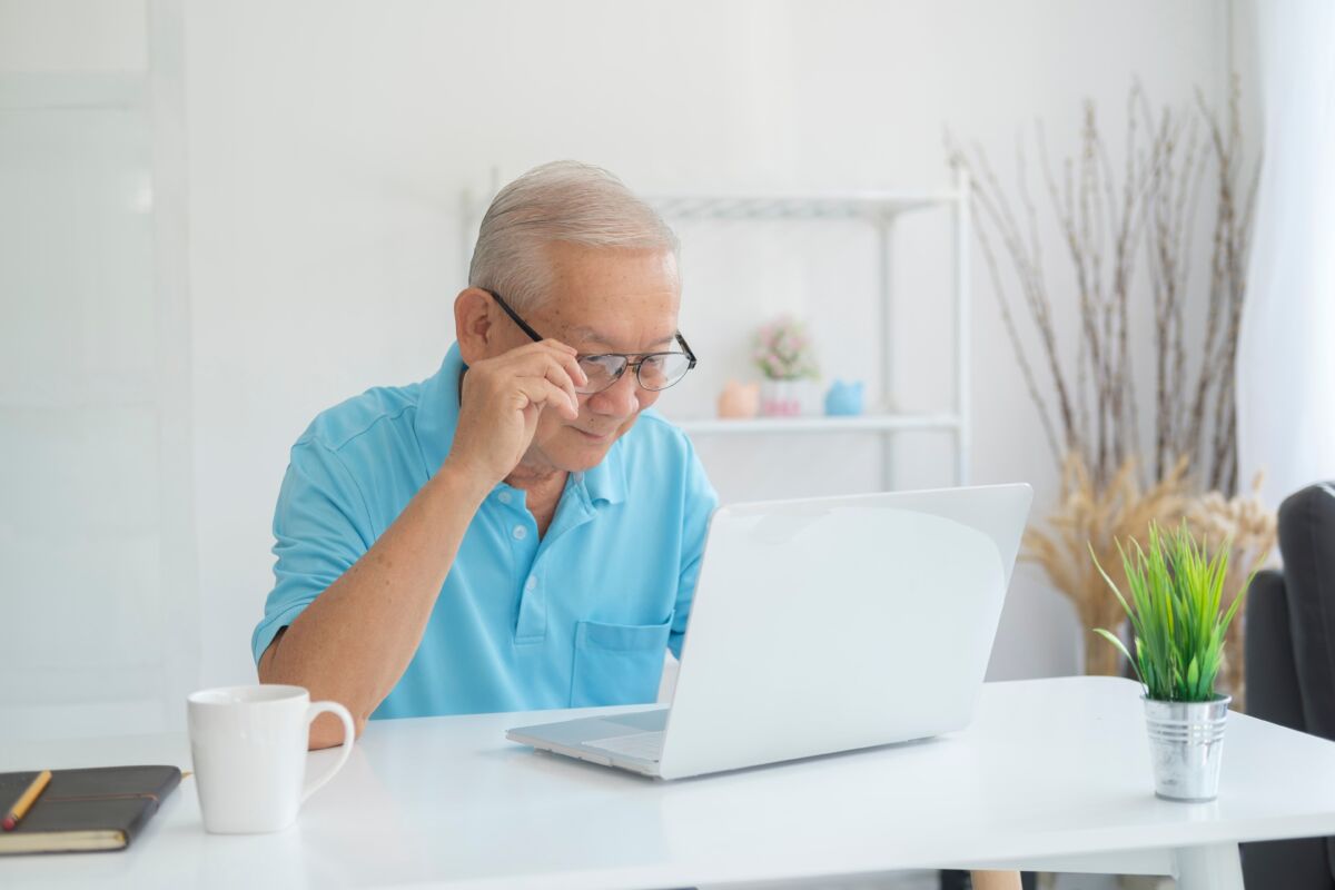 Senior man wearing glasses using a laptop at home, researching top rated Medicare Advantage plans in California for his upcoming healthcare enrollment.